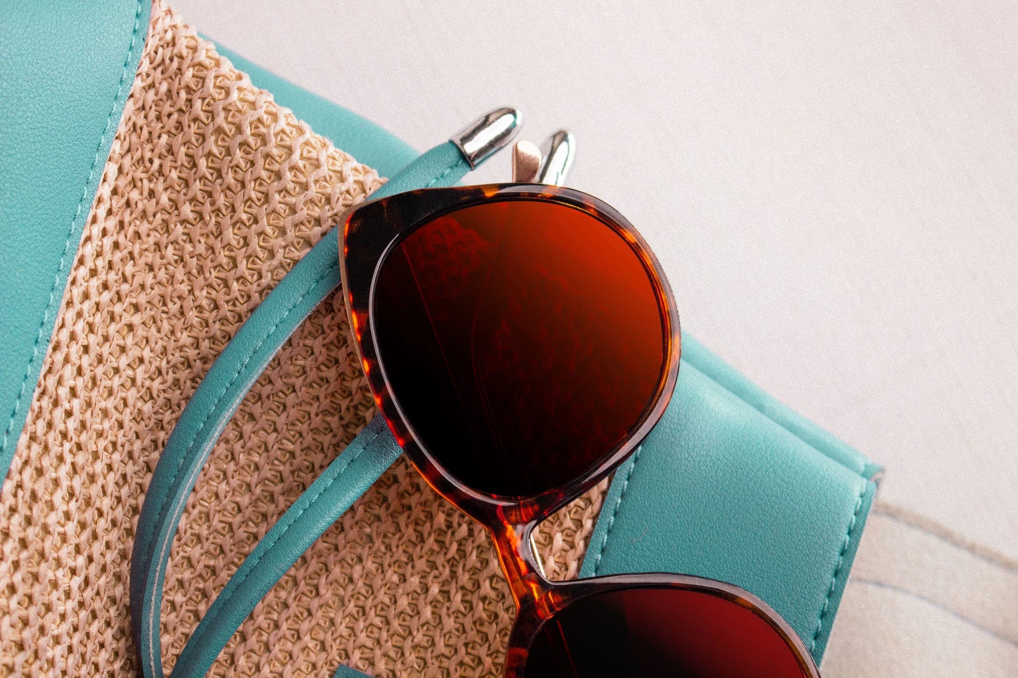 Tortoiseshell sunglasses resting on a woven straw bag with turquoise leather trim