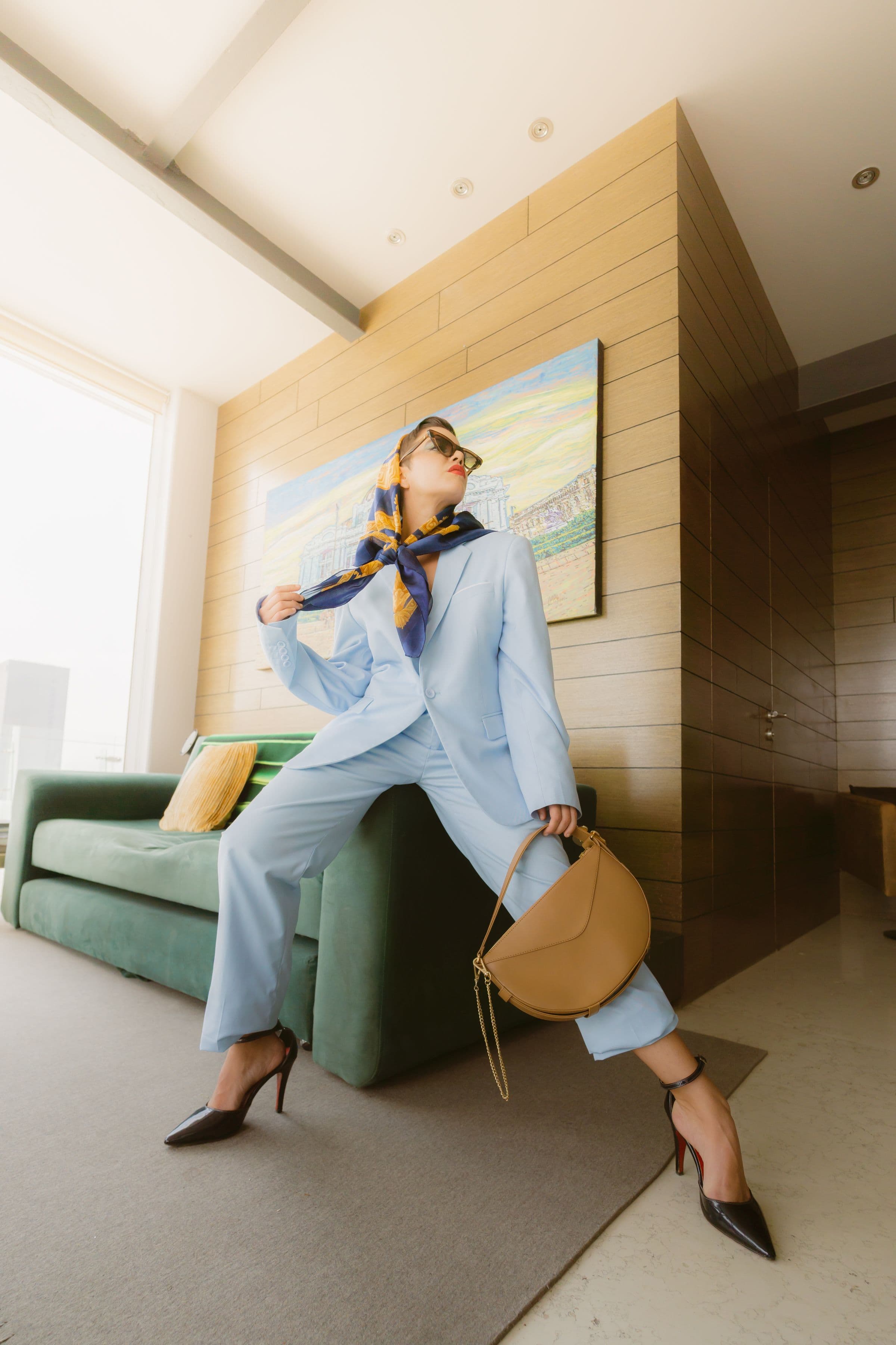 Woman in a pale blue suit with a silk head scarf and tan bag